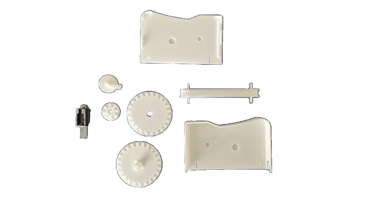 Nine cream-coloured printed parts laid out on a white surface: two shaped body plates, three toothed gears of different diameters, a cam, a guide rail and two small fixings.